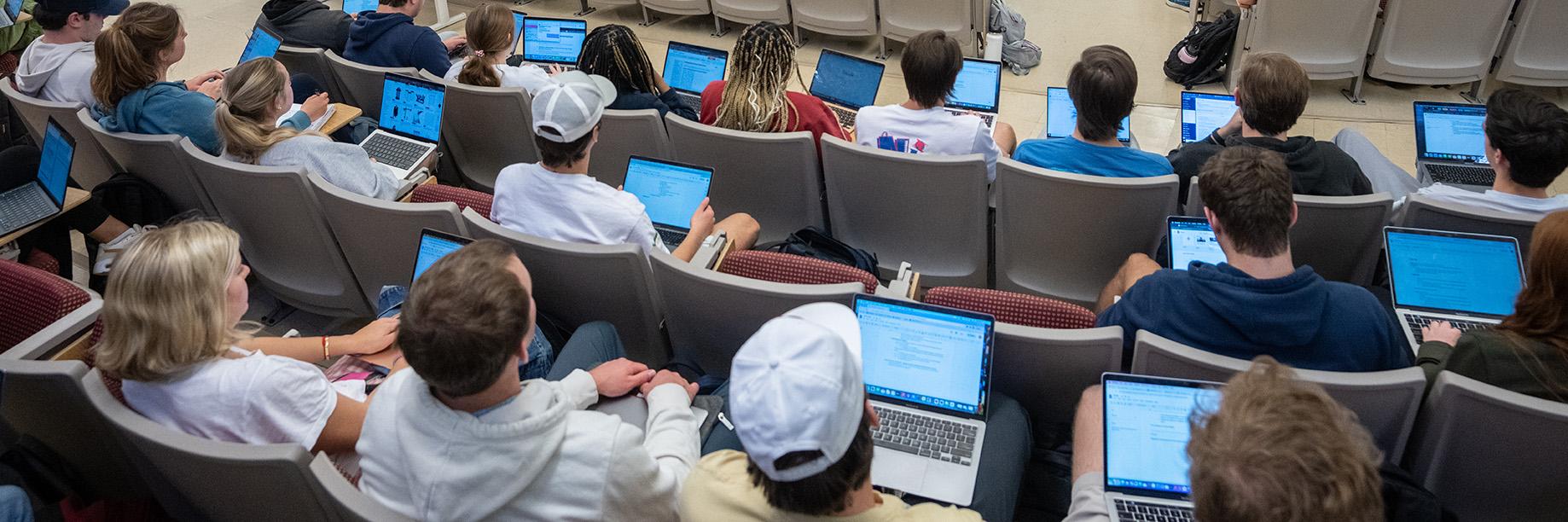 Students sitting in a lecture hall with laptops on their laps